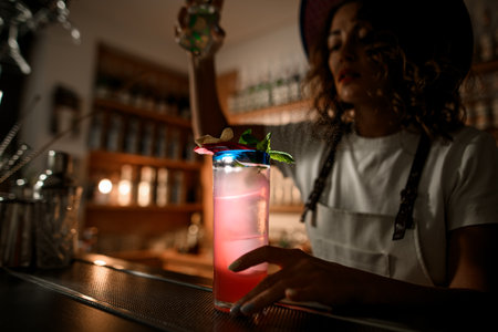Tall glass with a pink drink, illuminated by a light stands on the bar counterの写真素材