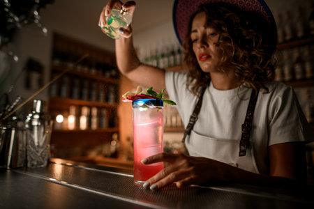 Female bartender prepares an exotic cocktail of pink color, decorated with leaves and peelの写真素材