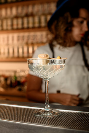 Glass with a transparent drink stands on the bar counter, on the rim of which lies a skewer with a piece of banana strung on itの写真素材