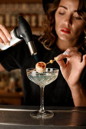 Female bartender holds a wooden skewer with a piece of banana strung on it, over a glassの写真素材