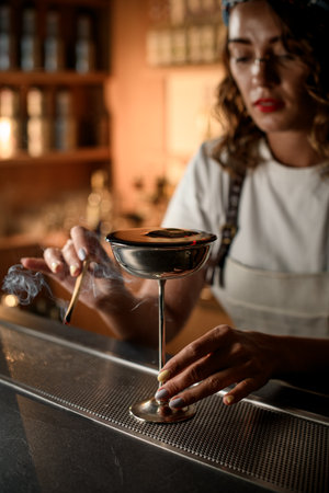 Focus on a metal glass with a tall thin stem filled with a cocktail, around which smoke from a wood chip spreadsの写真素材