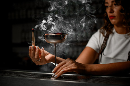 Female bartender holds a smoking wooden chip in her hand and looks at itの写真素材