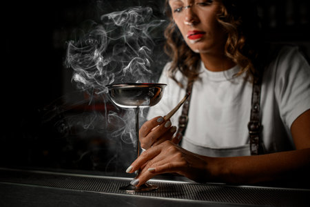 Front view of a female bartender placing a tall stemmed glass on the metal grate of the bar