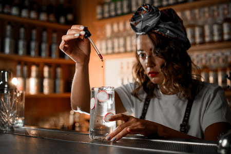 Female bartender drops brown drops with a pipette into a glass covered with condensation with a clear iced cocktailの写真素材