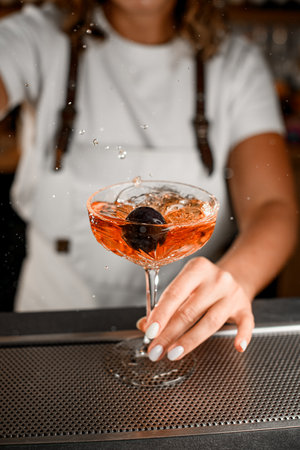 Female bartender holds a glass with a cocktail on the bar counterの写真素材