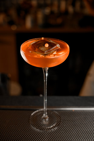 Beautiful glass with a tall thin stem filled with a cocktail with a huge ice cubeの写真素材