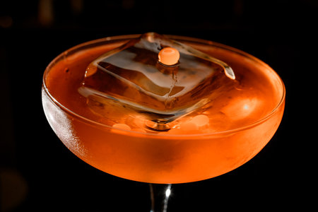 Close-up photo of the top of a glass filled with a brown cocktail with a huge ice cube that does not fit in the glassの写真素材