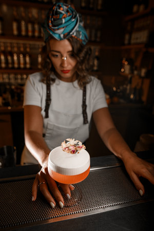Woman bartender holds a stem of a glass with a frothy cocktail, decorated with flower petals,の写真素材