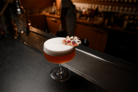 On the bar stands a glass with a thin stem, filled with a foamy cocktailの写真素材