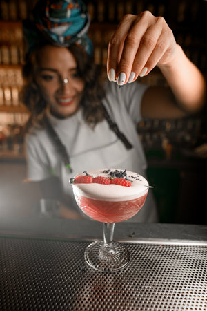 Happy female bartender sprinkles tea leaves on top of a foamy cocktailの写真素材