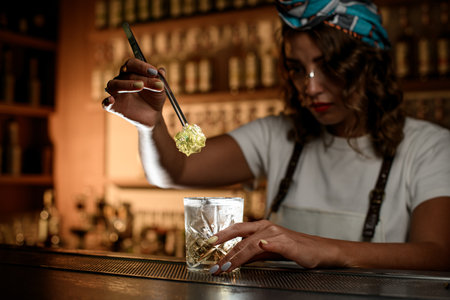 Female bartender holds a piece of marmalade with tweezers over a glass with a drinkの写真素材