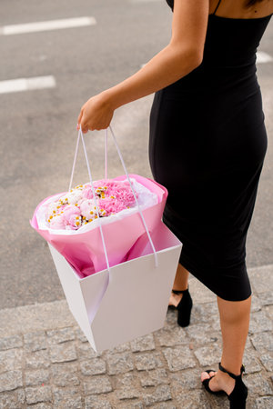 Graceful Bouquet. Girl in black dress holds beautifully adorned pink flowers.の写真素材