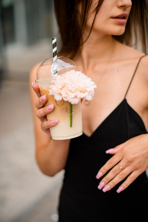 Black dressed girl holding a cocktail adorned with a delicate, vibrant flower.の写真素材