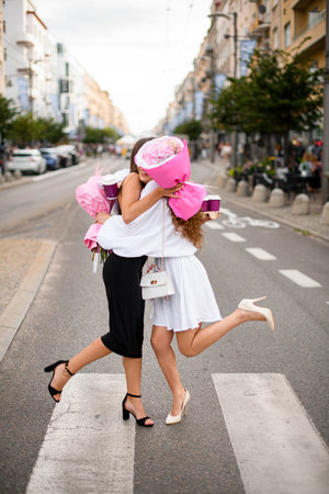 Meeting at Crossing. Girls with coffee and flower bouquet hugの写真素材