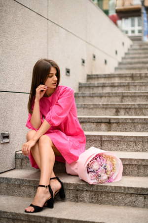 Seated on steps, a girl in pink admires a vibrant flower bouquet.の写真素材