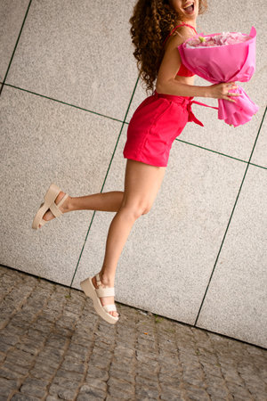 Curly haired girl jumps happily towards a vibrant bouquet of colorful flowers.の写真素材