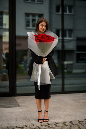 Girl smiles, holds large red rose bouquet by mirror buildingの写真素材