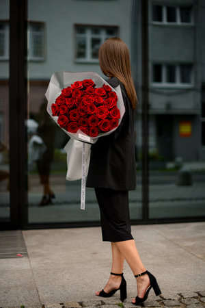 Brunette looks at buildings reflection, holding a massive bouquet of red rosesの写真素材