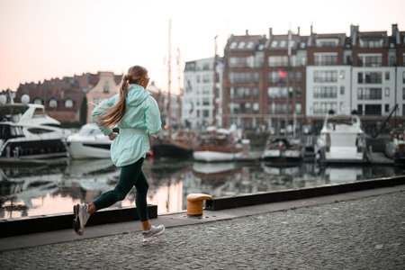 Back view of a young woman in a mint jacket and leggings running outdoorsの写真素材