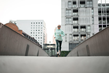 Rare motion shot of a young woman in a mint jacket running on an asphalt pavement and in flightの写真素材