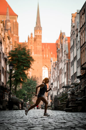 Female athlete jogging on the city sidewalk against the background of city buildingsの写真素材
