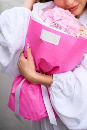 Happy woman hugging beautiful bouquet of gypsophila in pink paper, fixing her hairの写真素材