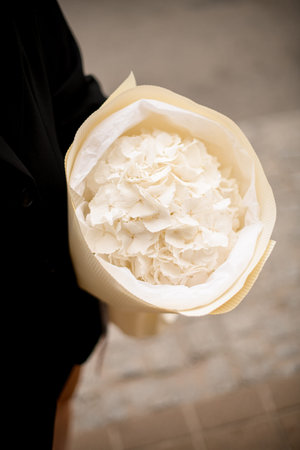 Chic bouquet of white flowers in hands of a girl standing on a city streetの写真素材