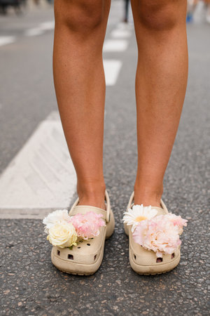 Crocs with flowers on a legs in a light beige color standing on a grey city streetの写真素材