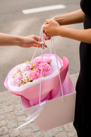 Hidden face of a slim girl standing on a city street with a pink and white bouquetの写真素材