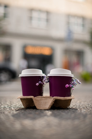 Purple glasses of coffee in cardboard stand and small pink lilac lavender and blue flowersの写真素材