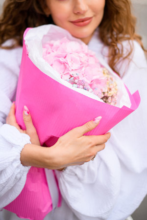Young girl with voluminous hair in a white dress with a mysterious bouquet of soft pink flowersの写真素材