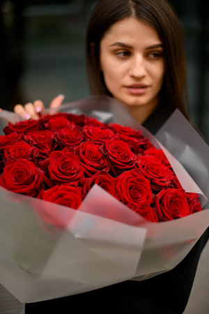 Young girl with beautiful face with a delightful bouquet of red rosesの写真素材