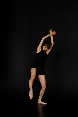 Young slim woman in black outfit with bare feet dancing in dance studioの写真素材