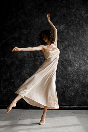 Slim woman in a light pink dress, dancing ballet, moving her arm and leg to one sideの写真素材
