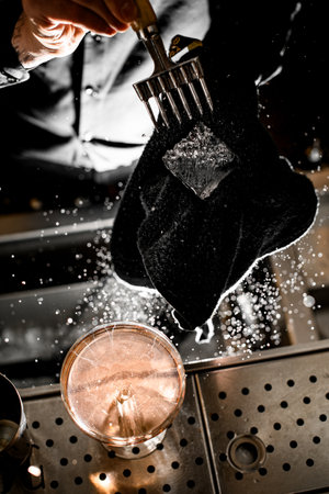 Stemmed glass with a brown cocktail and two parts of a shaker stand on a bar counterの写真素材