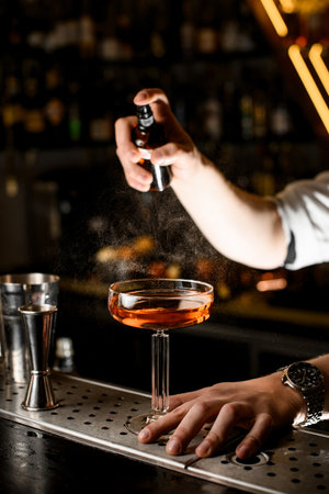 Male bartenders hand sprays a stemmed wine glass filled with a brown drinkの写真素材
