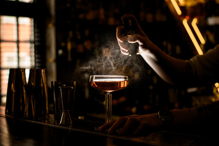 Bartenders hand sprays a glass with a brown cocktail, on the bar counterの写真素材