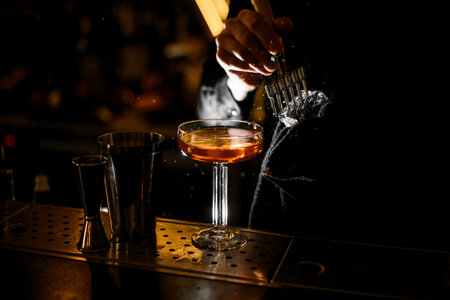 Bartender breaking an ice cube with an ice ax while holding ice with a towel over a glass of brown cocktailの写真素材