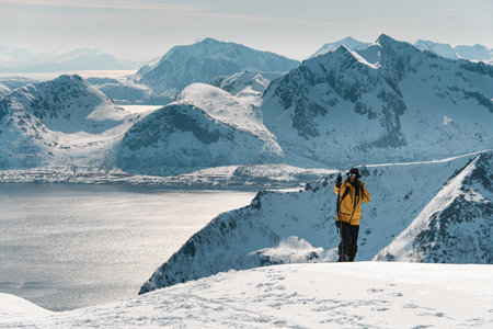 Tall person with one hand climbs to the top of the mountain, looking around at endless mountain landscapesの写真素材