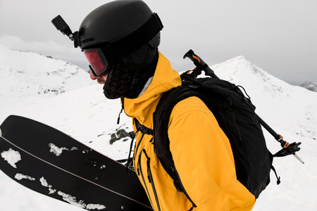 Side view close-up of one-armed skier in yellow jacket and helmet with video camera holding his splitboardの写真素材