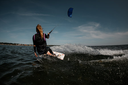 Back view girl in a wetsuit with stripes on a surfboard in the waterの写真素材
