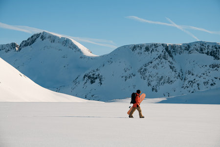 Side view of concentrated skier walking on snow carrying his splitboard in his handsの写真素材