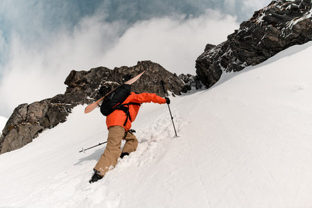 Bottom view close-up of a skier climbing a slope, carrying his skis on his shoulders