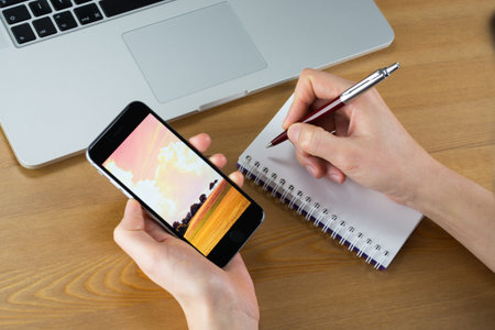 Writing notes and watching smartphoneの写真素材