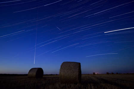 Hay bale at night with star trails in the sky.Star movement is caused by Earth's rotation and camera's long exposure.の写真素材