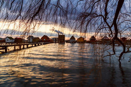 Sunset lake Bokod with pier and fishing wooden cottages, power plant in background, Hungaryの写真素材