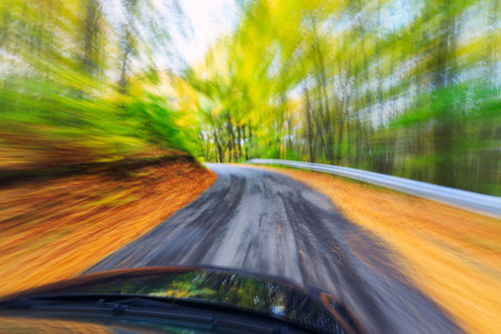 Car driving fast into autumn forestの写真素材