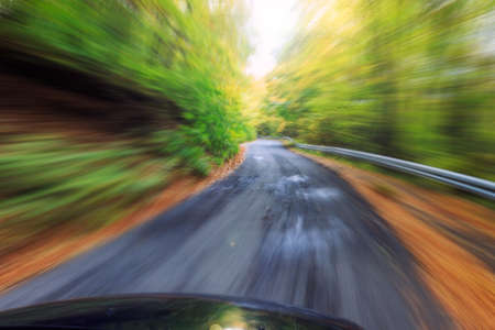 Car driving fast into autumn forestの写真素材