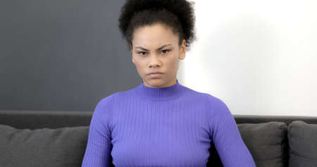 Sad African American woman is sitting on the sofa. Young black woman resting at home.の写真素材