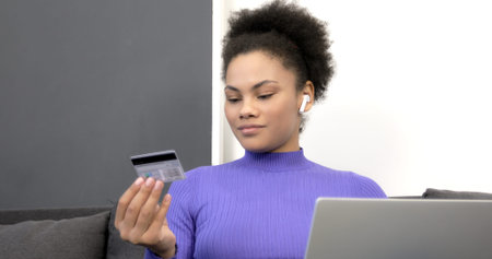 An African American model uses a credit bank card and enters a number on a computer. Black woman...